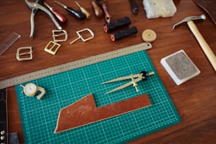 Leatherworking station with various tools on wooden table, copy space