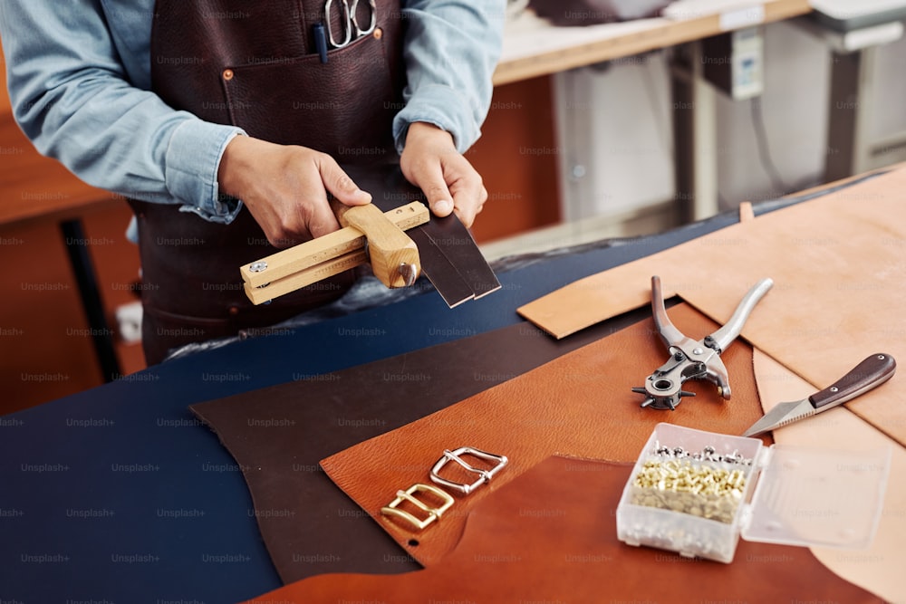 Closeup of modern artisan creating handmade pieces in leatherworking shop, copy space