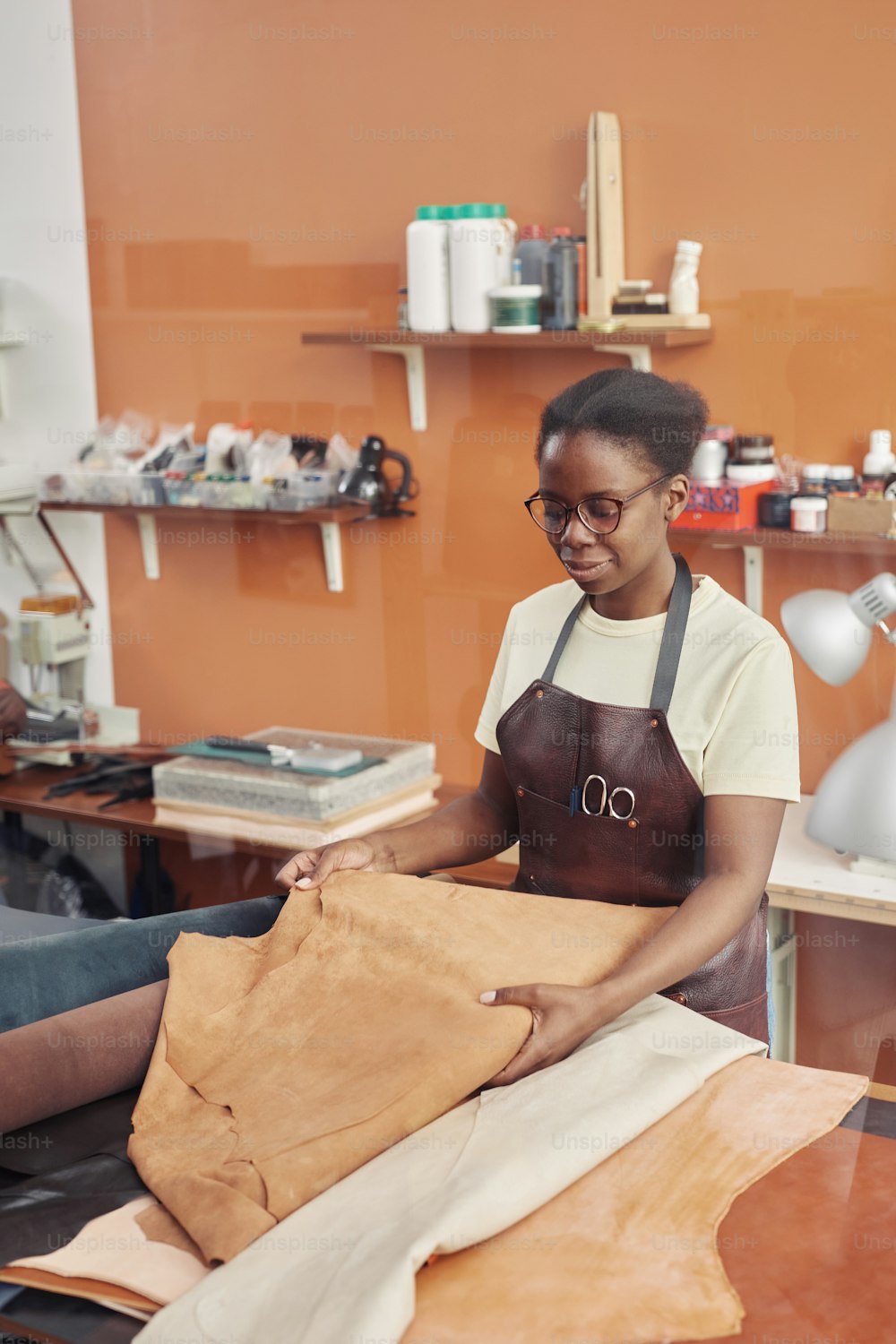 Vertical portrait of young black woman working with leather and creating handmade pieces in workshop