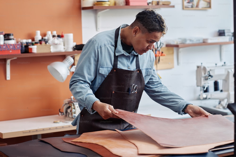 Vue latérale portrait d’un jeune artisan inspectant le cuir dans l’atelier et créant des pièces faites à la main, espace de copie