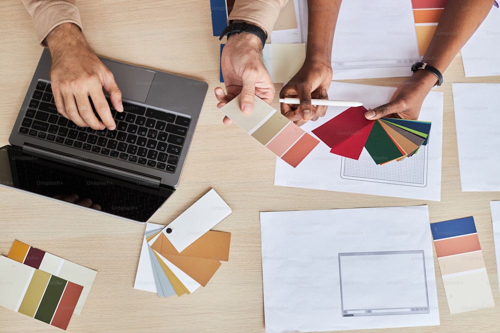 Top view at two designers choosing color swatches while working on UI project in office