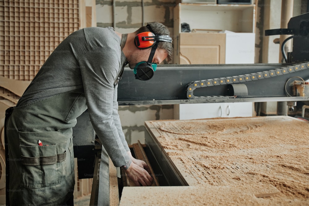 木工生産で機械を操作する際に完全な保護服を着た男性労働者の側面図のポートレート