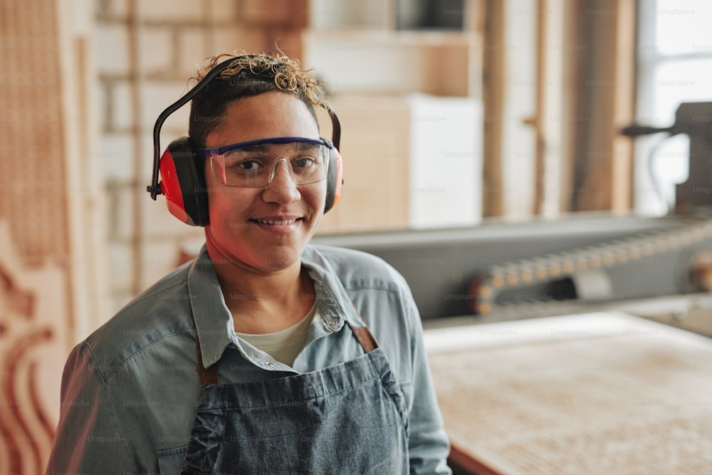 Portrait of female worker smiling at camera while wearing noise cancelling headphones in workshop, copy space