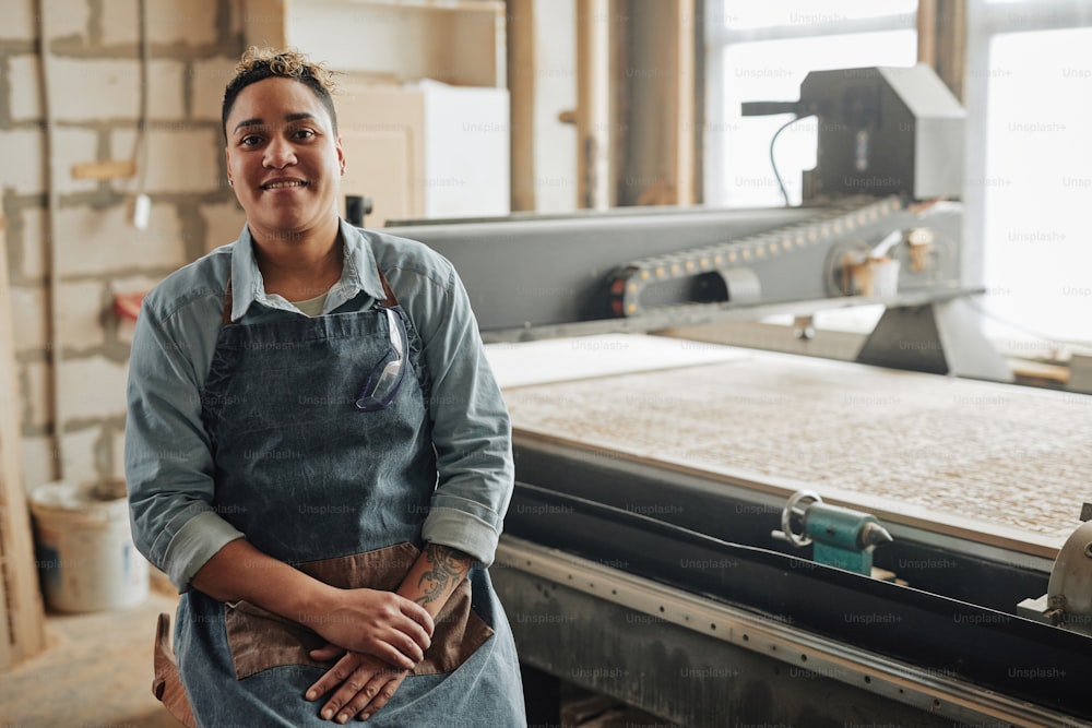 Porträt einer lächelnden Arbeiterin, die in die Kamera schaut, während sie an der Holzschneidemaschine in der Werkstatt posiert, Kopierraum