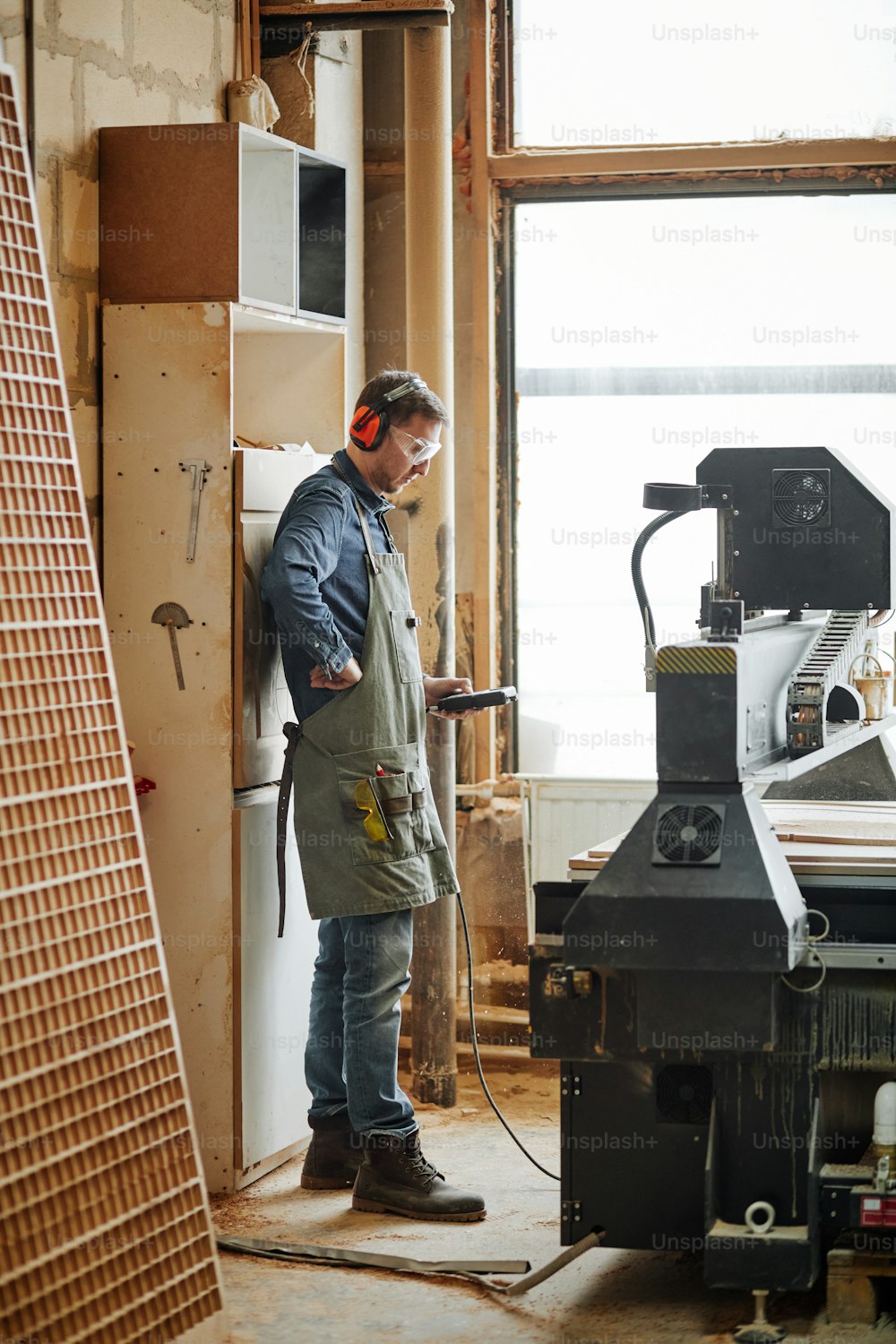 Ritratto a figura intera del falegname maschio che opera la macchina da taglio del legno nell'officina di produzione automatizzata