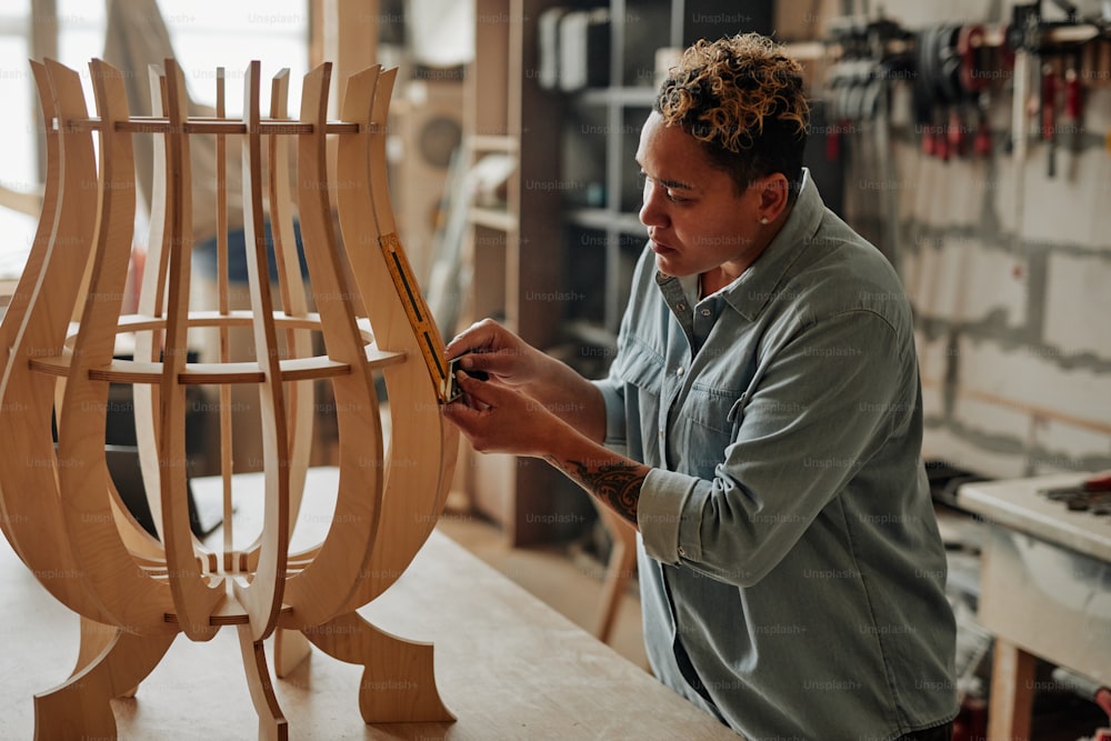 Side view portrait of modern female carpenter designing wooden furniture piece in workshop interior