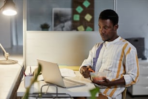 Portrait of young African American man eating healthy snack while working or studying late at night