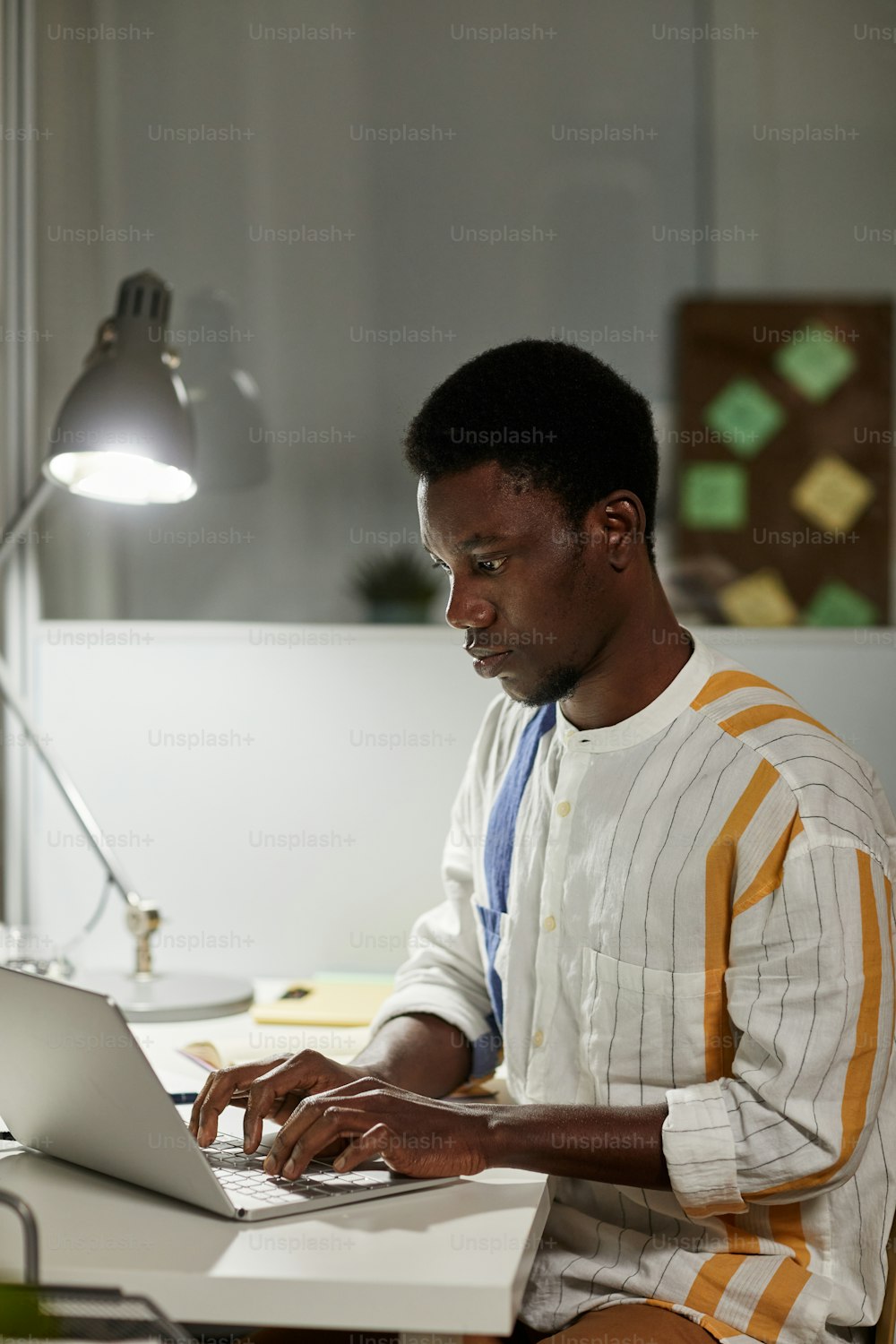 Vertical side view portrait of young African American man studying or working late at night