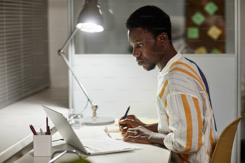 Minimal side view portrait of young African American man studying late at night, copy space