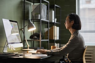 Retrato de vista lateral del diseñador de software asiático que usa la computadora mientras trabaja hasta tarde en la oficina en casa, copie el espacio