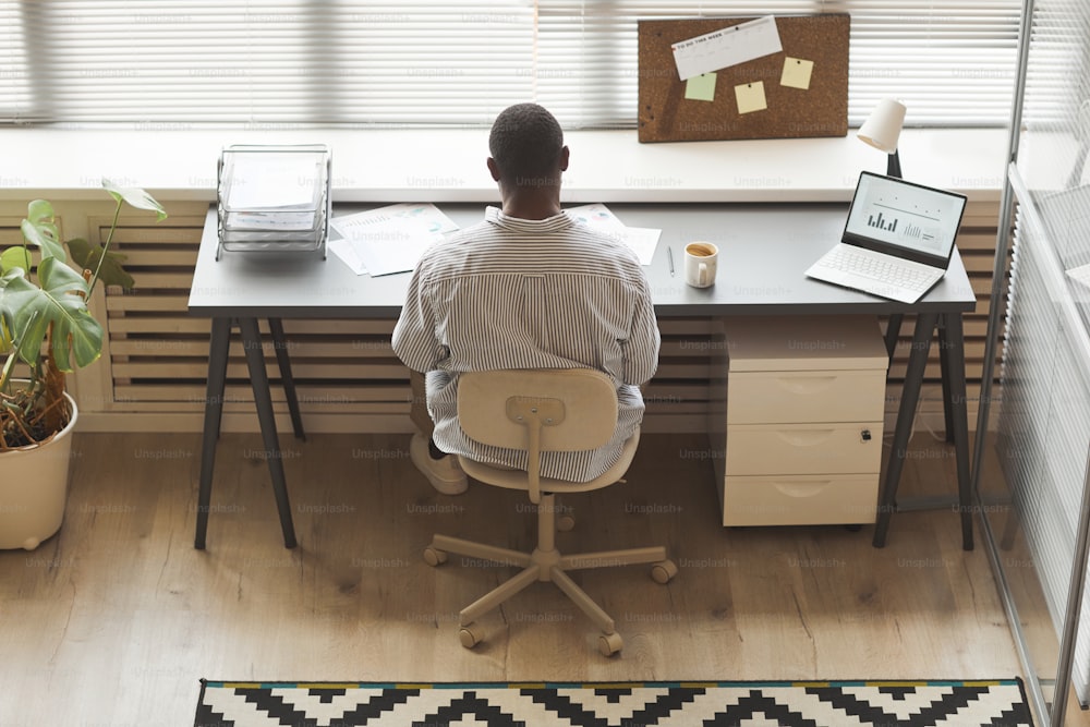 Minimale Draufsicht auf einen schwarzen Unternehmer, der Dokumente analysiert, während er am Fenster im Büro arbeitet, Kopierraum