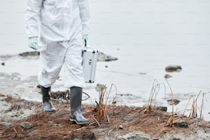 Tiefschnittaufnahme einer nicht wiederzuerkennenden Person in Schutzanzug, die am Wasser an einem ökologischen Katastrophenort vorbeigeht, Kopierraum