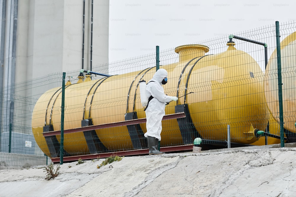 Wide angle view at worker wearing protective suit disinfecting industrial area, copy space