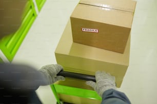 Gros plan d’une personne portant des gants portant un chariot avec des boîtes en carton