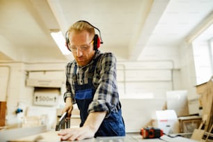 Retrato de cintura para arriba de carpintero contemporáneo cortando madera mientras trabaja en carpintería, espacio de copia