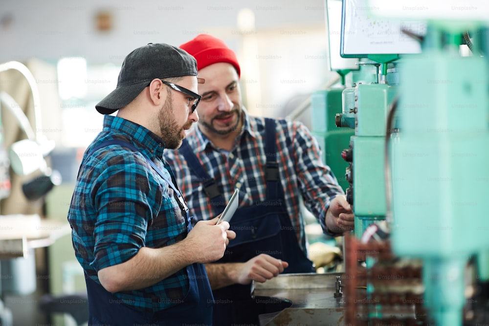 Side view portrait of mature factory workers training new employee explaining operation of machine units in workshop, copy space