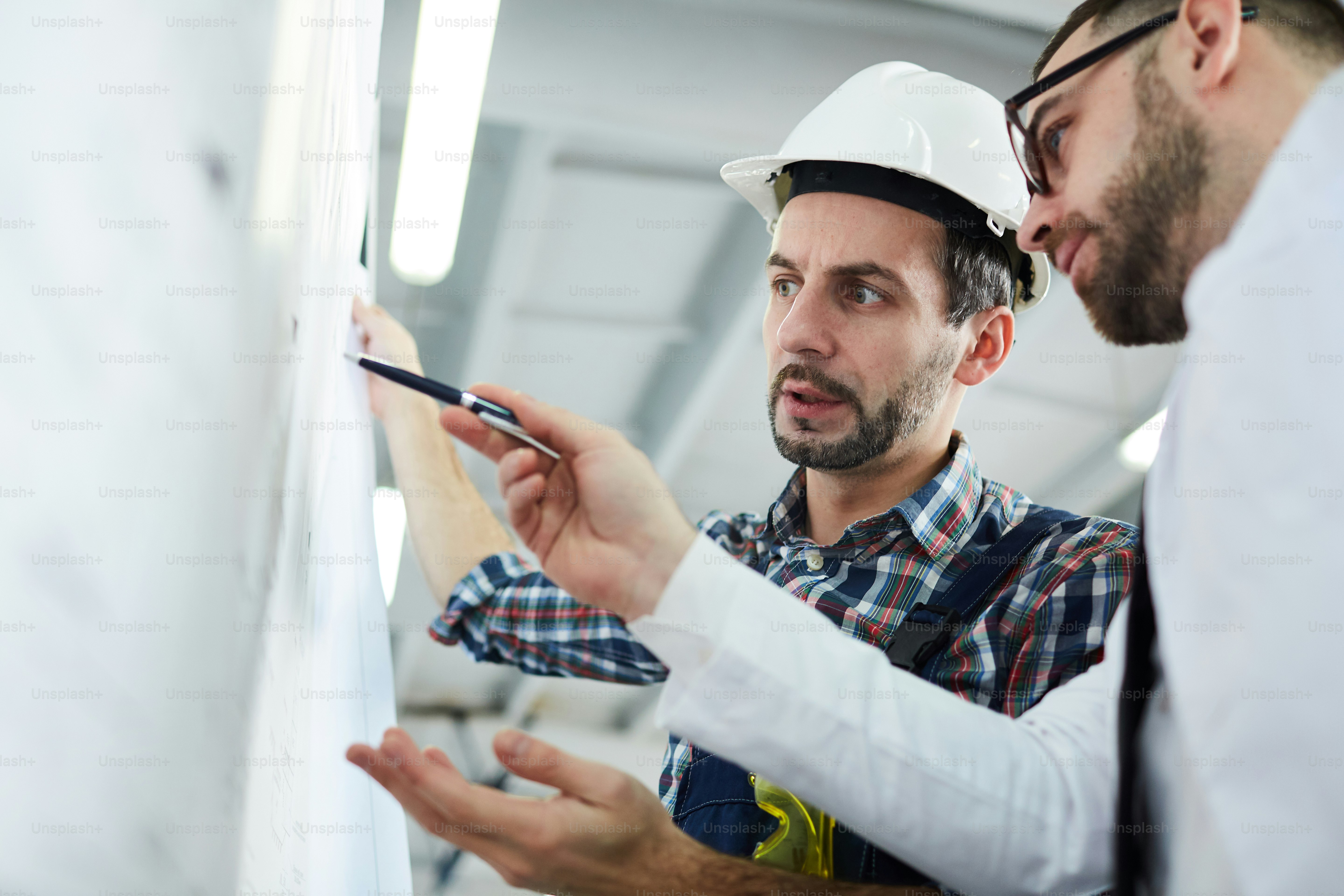 Low angle portrait of two factory workers discussing  plans standing in workshop, copy space