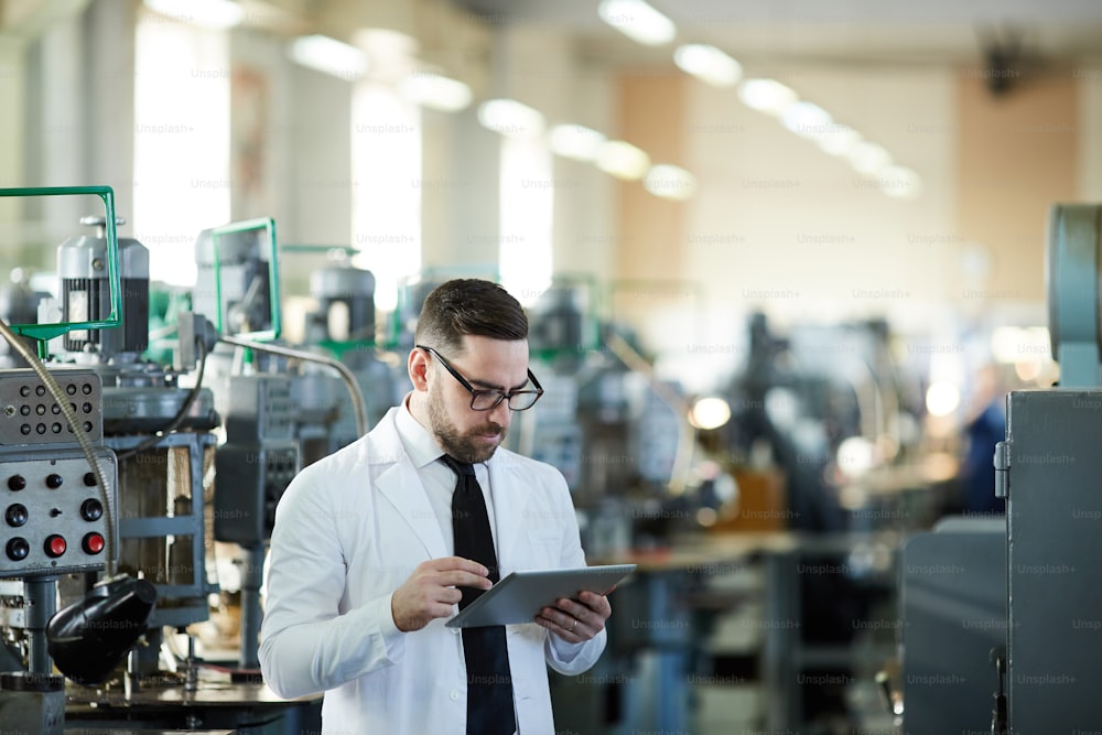 Porträt eines gutaussehenden Fabrikarbeiters in Laborkittel mit digitalem Tablet in Industriewerkstatt, Kopierraum