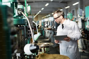 Side view portrait of senior quality inspector wearing lab coat checking industrial machine units in factory workshop, copy space