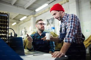 Portrait of two mature factory workers discussing production standing at workplace, copy space