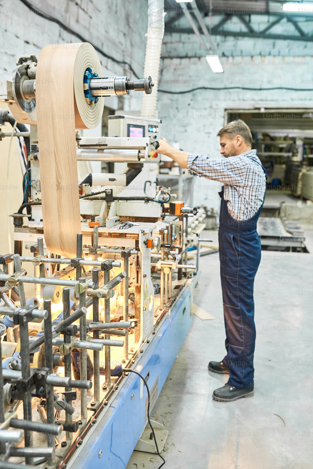 Full length portrait of mature factory worker placing sheet of wood on machine in modern workshop, copy space