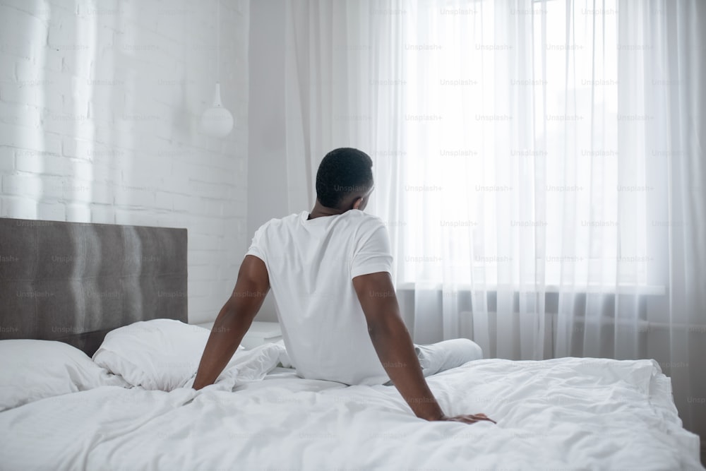 Manhã. Homem afro-americano sentado na cama e se alongando