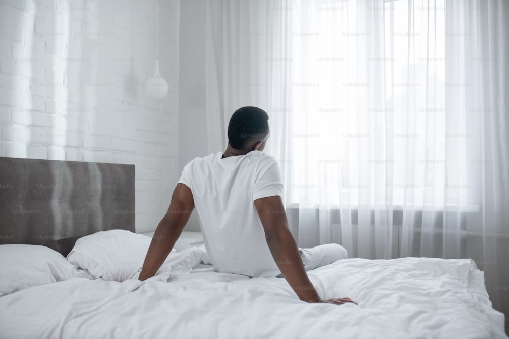 Morning. African american man sitting on bed and stretching