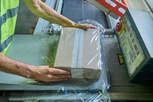 Foto recortada de um operador de casa de estoque envolvendo a caixa de papelão usando a máquina de embalagem de celofane