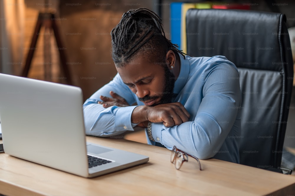 Un jeune employé de bureau afro-américain épuisé somnolent sur la table devant son ordinateur portable