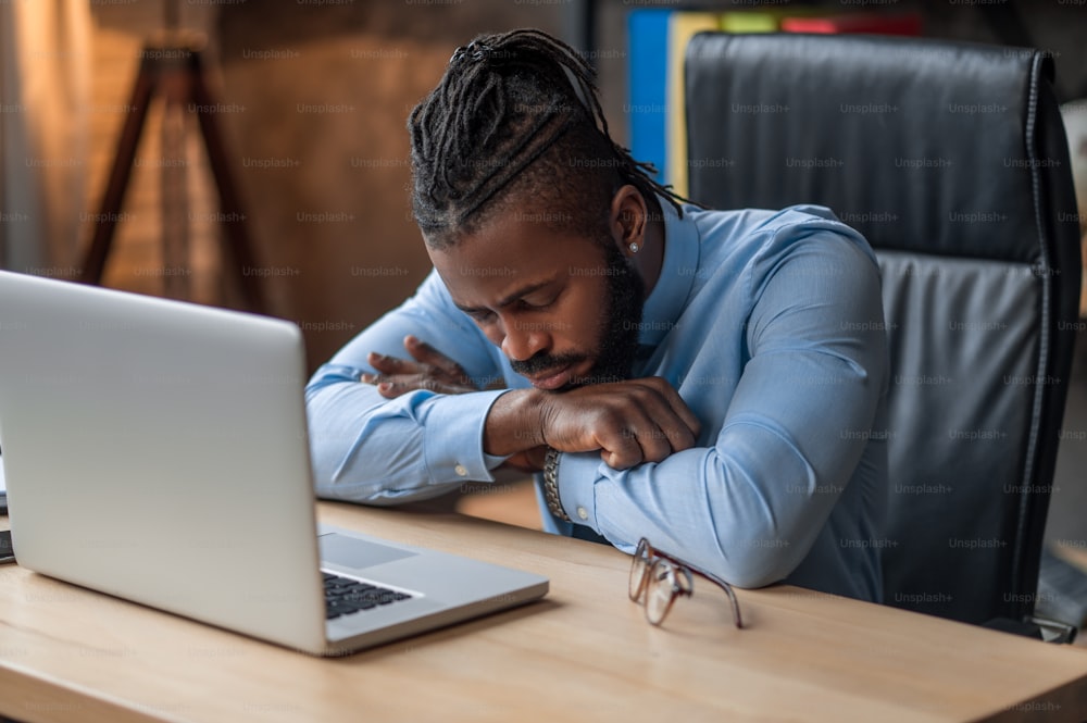 Exhausted young African American office worker dozing on the table in front of his laptop