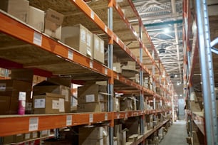 Narrow aisle in a storage area with numerous cardboard boxes arranged on the stainless steel racks
