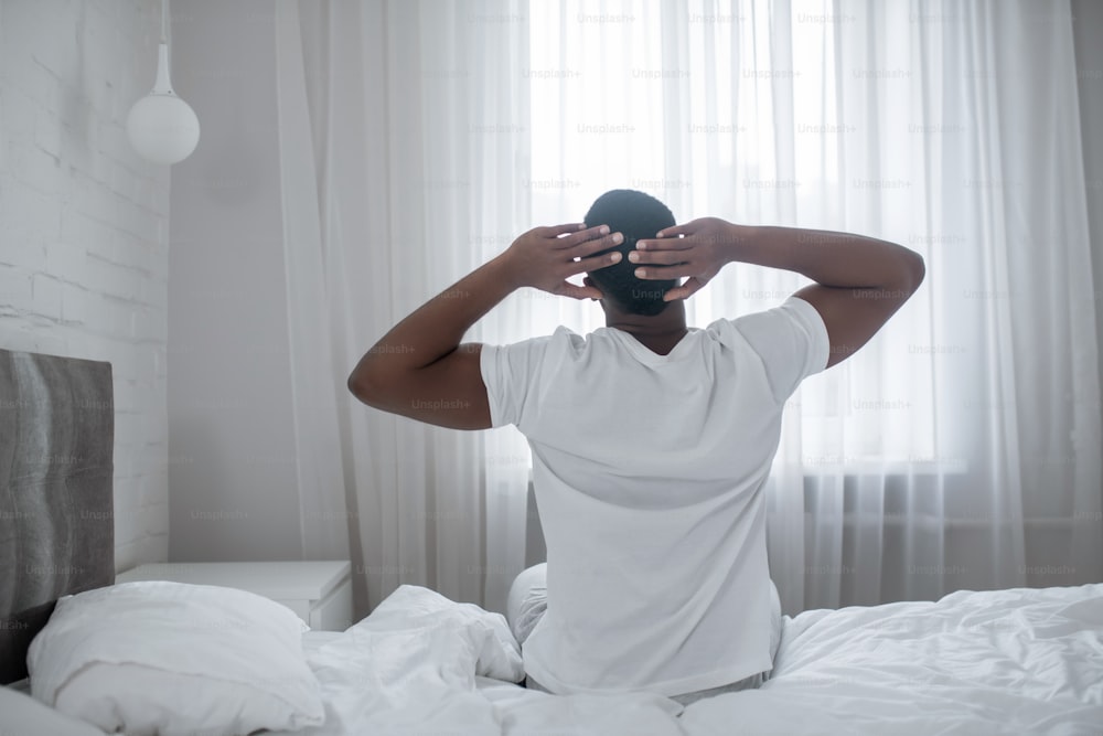 Morning. African american man sitting on bed and stretching