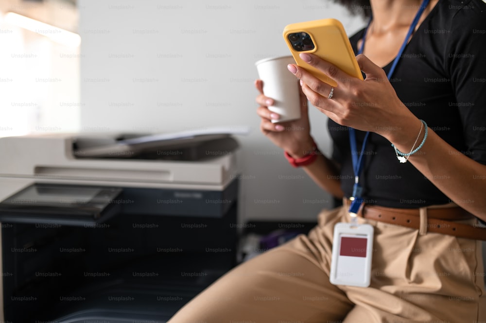 Texting. Woman sitting in the office with a phone and cup with coffee in hands