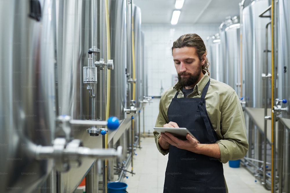 Craft beer brewery worker with tablet computer checking equipment