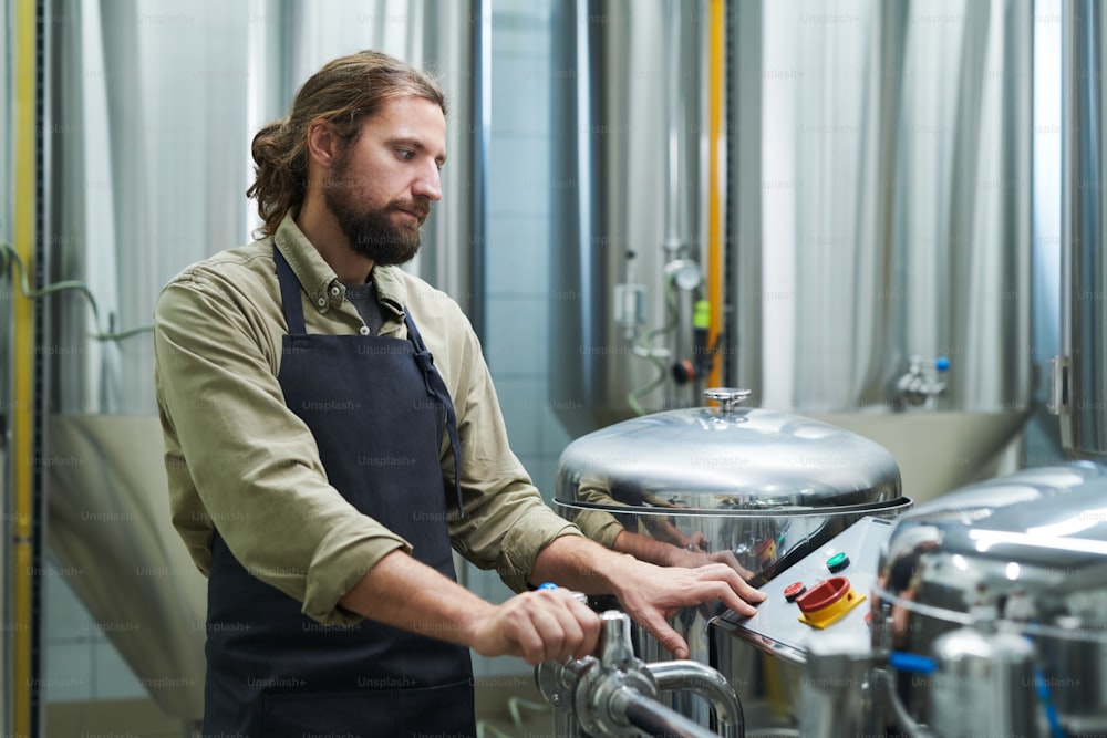 Trabajador de la cervecería mirando la pantalla pequeña al establecer la presión adecuada para el proceso de fermentación