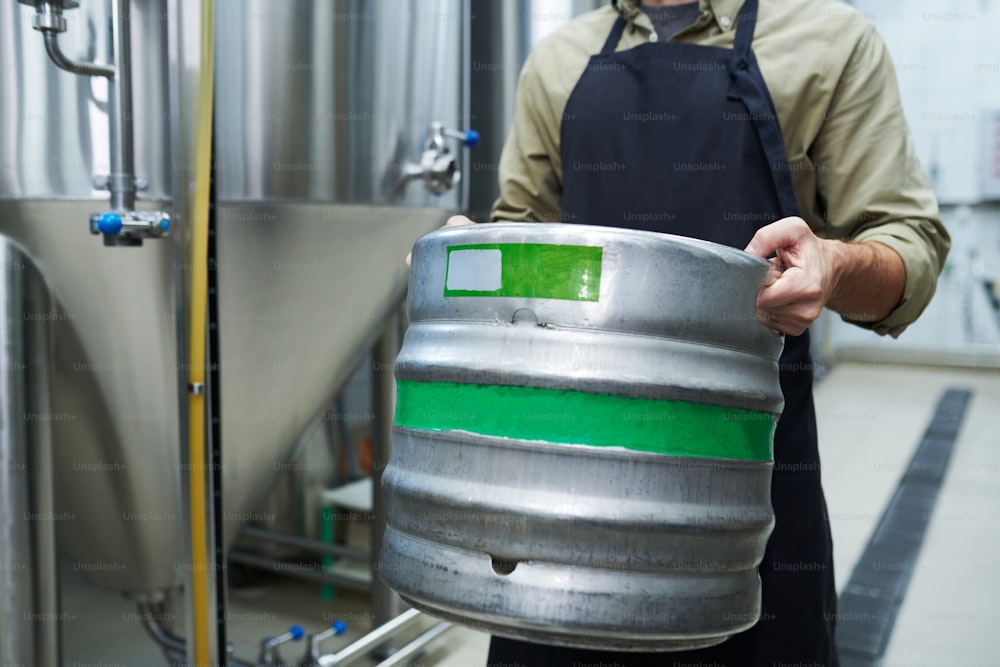 Trabajador de microcervecería que lleva barril pesado con cerveza, concepto de pequeña empresa