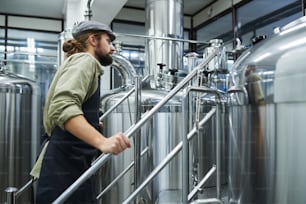 Brewery owner in flat cap and apron checking equipment