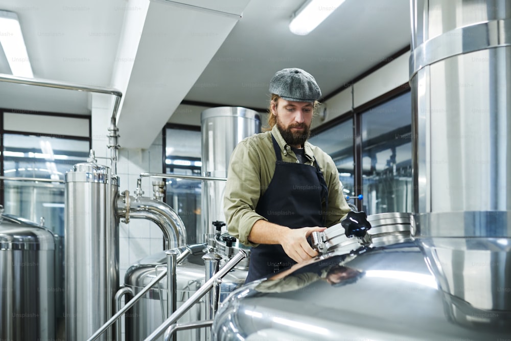 Pequeno trabalhador de cervejaria verificando tanques com cerveja fermentada