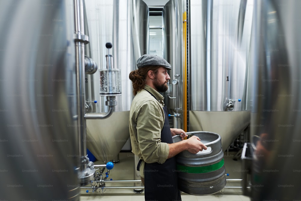 Side view of private brewery worker carrying keg of beer