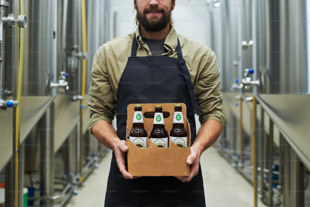 Imagem recortada de cervejeiro sorridente mostrando cerveja engarrafada produzida em sua cervejaria