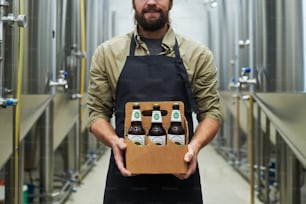 Cropped image of smiling brewer showing bottled beer produced in his brewery