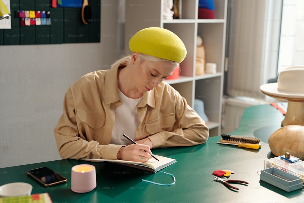 새로운 계절 패션 컬렉션을 작업하는 동안 노트북에 새로운 모델의 스케치를 연필로 그리는 젊은 창조적인 여성