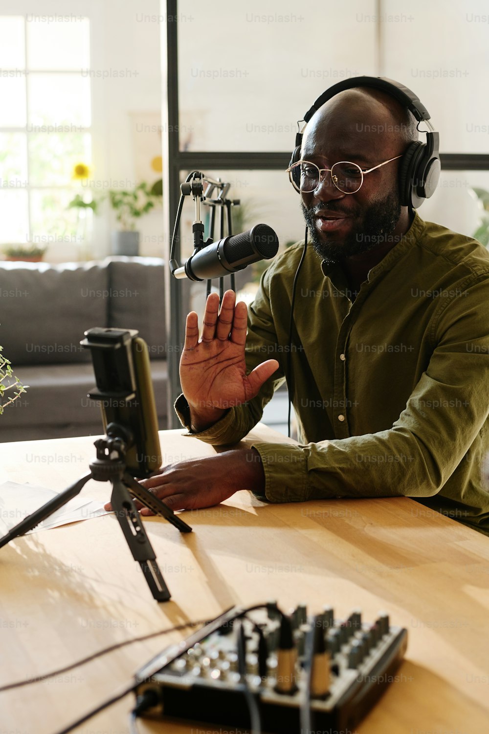 Young male blogger or host in casualwear waving hand to his online audience and looking in smartphone camera during livestream