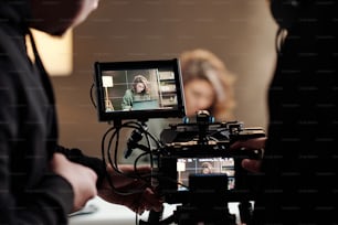 Primer plano de pantallas steadicam con modelo femenina usando computadora portátil por mesa durante el comercial filmado por el camarógrafo y su asistente