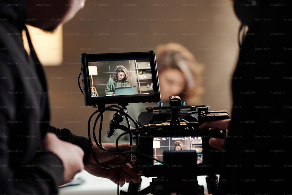 Close-up de telas steadicam com modelo feminino usando laptop por mesa durante o comercial sendo filmado pelo cinegrafista e seu assistente