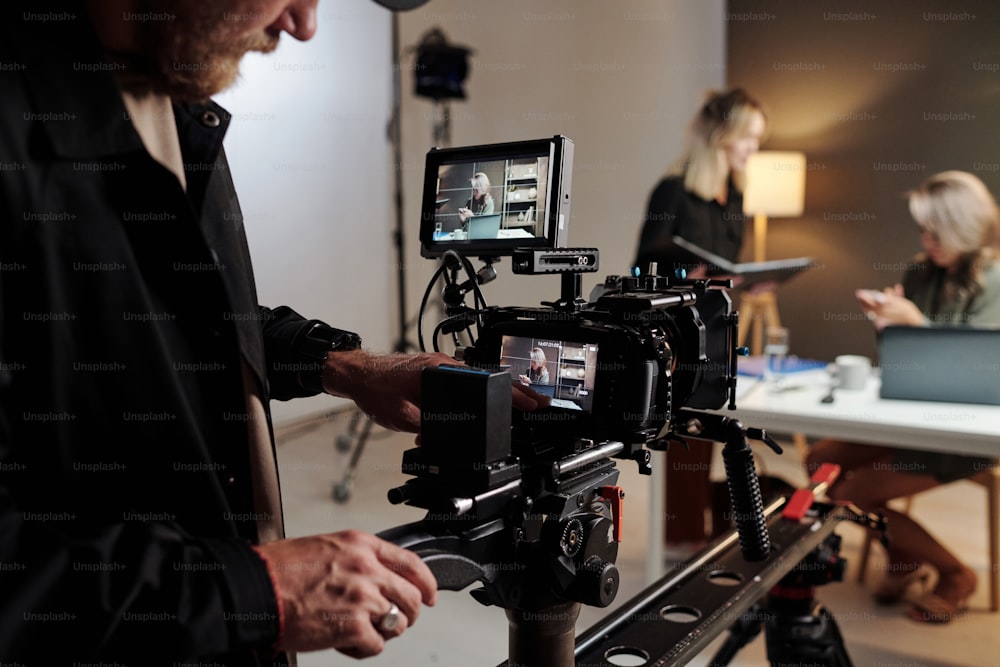 Jeune homme avec caméra vidéo debout dans le studio devant son assistante avec des documents et un modèle féminin participant à un tournage commercial