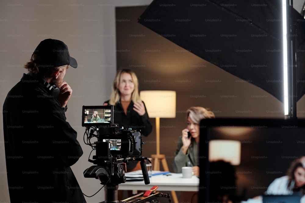 Rückansicht eines jungen Videofilmers, der während der Dreharbeiten zu einem Werbespot mit weiblichem Model im Studio vor Steadicam steht