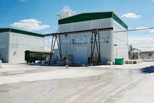 Two small white buildings of modern production factory standing in wide yard with blue sky and clouds above on sunny summer day