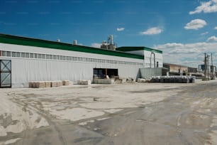 Parte della lunga costruzione di una moderna fabbrica industriale di colore bianco in piedi lungo un ampio cortile asfaltato da qualche parte in periferia