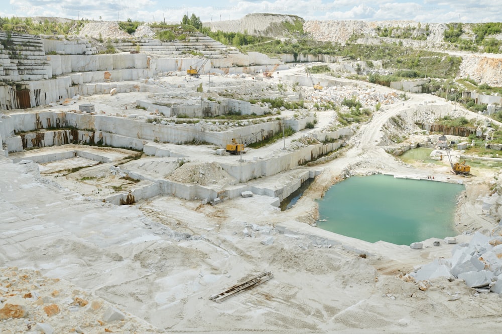 Vista acima de parte do vasto território da pedreira moderna pertencente à fábrica de produção industrial com pequena lagoa e maquinário